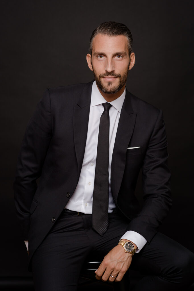 Portrait professionnel d’un homme d’affaires élégant en costume noir et cravate, représentant le leadership, la confiance et le professionnalisme.