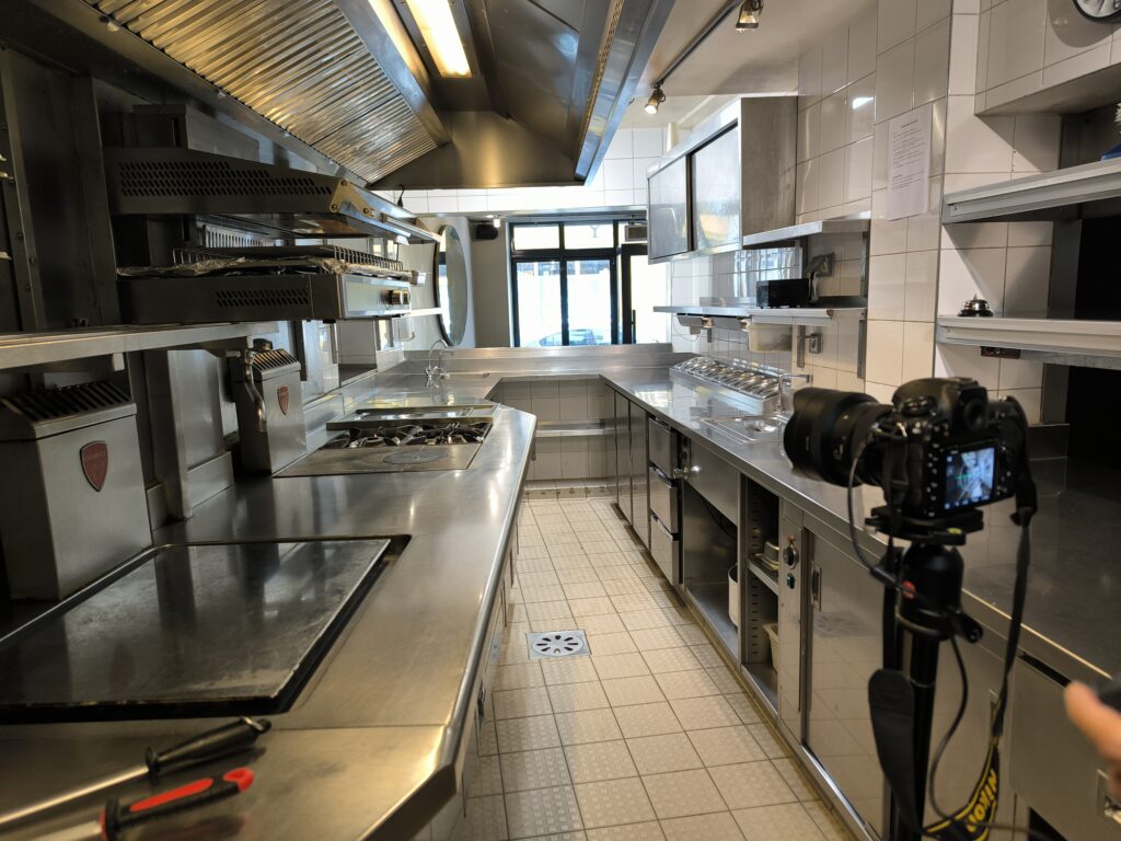 Cuisine professionnelle en inox avec un appareil photo sur trépied au premier plan.