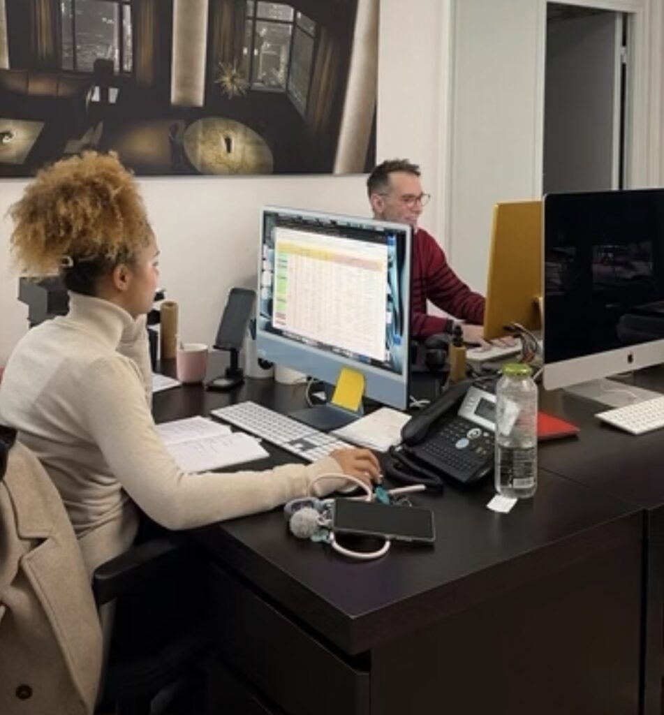 Une collaboratrice et un collaborateur travaillant côte à côte sur des ordinateurs de bureau de type iMac dans un espace de travail corporate moderne.